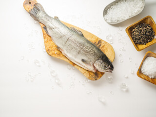 One fresh fish on a wooden cutting board. Salt, spices. White background. High angle view. The concept is cooking dishes from fish and seafood, restaurant, hotel, cafe, home cooking, culinary blog.