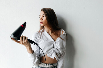 Thoughtful young woman thinking and drying her straight long brunette hair on white background. Woman is getting ready for work