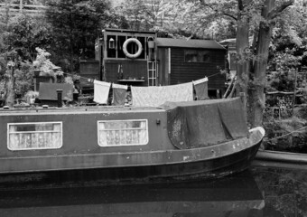 an old scruffy blue narrow boat moored next to wooden sheds with washing on the line on the rochdale canal near hebden bridge