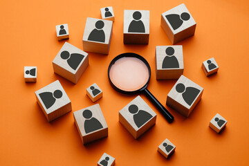 Wooden cubes with the image of a man lie next to a magnifying glass on an orange background. The...