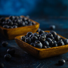 Fresh blueberries in square yellow bowls. Dark blue background. Harvest festival, farming, forestry, agriculture. Cooking, healthy food. Ecology. Environmental protection.