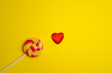 Multicolored round lollipop on yellow background. Heart nearby. Top view. Space for copying....