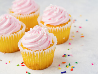 Festive composition - multi-colored confetti are scattered on a white tablecloth. Lots of cupcakes with pink berry cream. Birthday, gifts, surprises, sweet food. Restaurant, hotel, bakery.