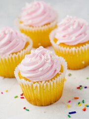macro photography. Cupcakes with protein berry pink cream, multi-colored confetti are scattered on a white background. Romantic date, birthday, anniversary, family holiday.