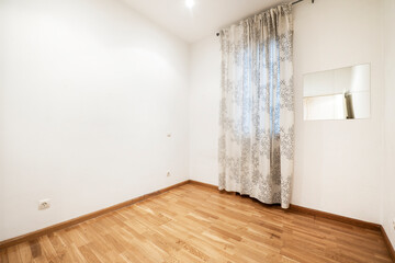 Empty room with oak hardwood floor, window covered by curtain and mirror on the wall
