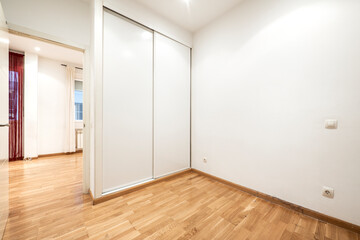 Empty room with built-in wardrobe with white sliding doors with oak wood flooring