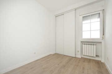 Fototapeta na wymiar Empty room with light wooden floor, white wooden sliding wardrobe doors and aluminum window above aluminum radiator