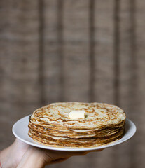 A woman's hand holds a stack of pancakes with a piece of butter. Selective focus.