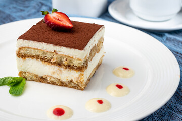 classic tiramisu dessert with mint and strawberry on white plate - 482090924