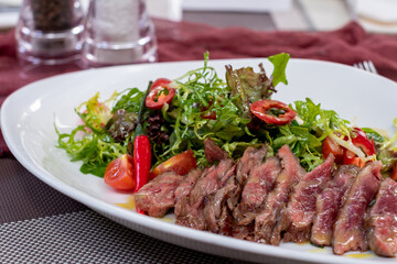 Steak salad with beef and vegetables on a white plate