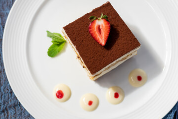 classic tiramisu dessert with mint and strawberry on white plate - 482090987
