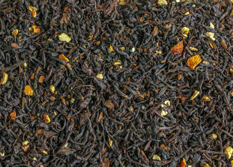 Background of aromatic black tea leaves with dried citrus slices and peel. Dry black tea texture