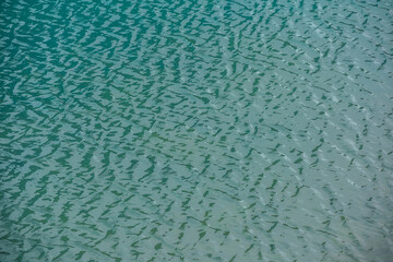 Scenic nature background of relaxing shiny ripples on calm water of alpine lake. Simple fragment of meditative turquoise lake clear water surface. Minimalist nature texture of mountain lake water.