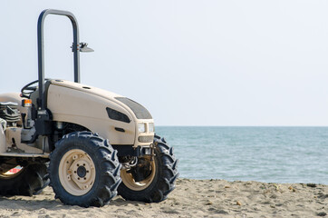 Tractor on the beach, symbol of work and summer jobs with the sea background, used for cleaning the sand, beach, and various jobs. vehicle without logos.