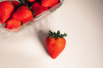 red strawberry on white table with plastic carton of strawberries