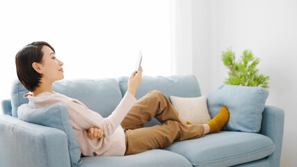 ソファーに座りながらスマートフォンを使う若い女性