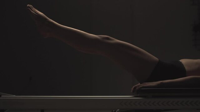 Young fit athletic girl exercising while jumping on pilates reformer machine with moving platform on tension springs
