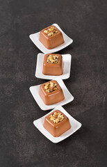 Small chocolate nut cream dessert in the shape of a square savarin on a plate on a dark gray background. Top view