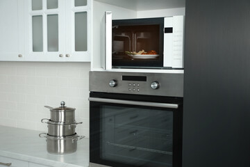 Fototapeta premium Open microwave oven with food on white shelf in kitchen