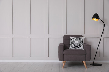 Grey armchair and lamp near empty molding wall indoors, space for text