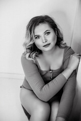 Naklejka premium Girl dressed in bodysuit. Black and white portrait of young beautiful plus size woman indoor. Body positive. Attractive plus-size woman with curvy hair. Chic of natural beauty. Film grain. Femininity