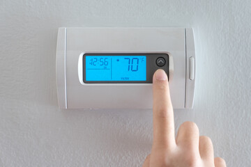 A woman is pressing the down button of a wall attached house thermostat with digital display showing temperature 70 degree Fahrenheit for heating, cooling, electricity and gas saving - obrazy, fototapety, plakaty
