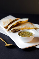 chicken quesadilla with cheese and guacamole, along with green hot sauce