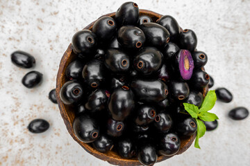 Black ripe Syzygium cumini fruits. Dark black java plum in a wood bowl at isolated white background. Green mint leaf on top of some large java plums.