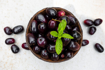 Dark pink-red ripe Syzygium cumini fruits. Dark black java plum in a wood bowl at isolated white background. Green mint leaf on top of some large java plums.