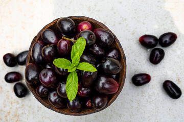 Dark pink-red ripe Syzygium cumini fruits. Dark black java plum in a wood bowl at isolated white background. Green mint leaf on top of some large java plums.