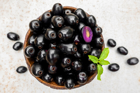 Black ripe Syzygium cumini fruits. Dark black java plum in a wood bowl at isolated white background. Green mint leaf on top of some large java plums.