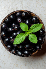 Black ripe Syzygium cumini fruits. Dark black java plum in a wood bowl at isolated white background. Green mint leaf on top of some large java plums.