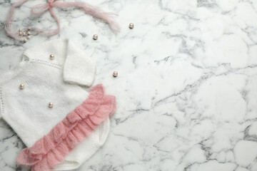 Cute knitted baby bodysuit on white marble background, top view. Space for text
