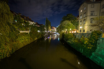 Fototapeta na wymiar Panorama of Ljubljanica river in the city center of Ljubljana with a bridge in background in summer, during a night evening. it is a symbol of the capital city of Slovenia.....
