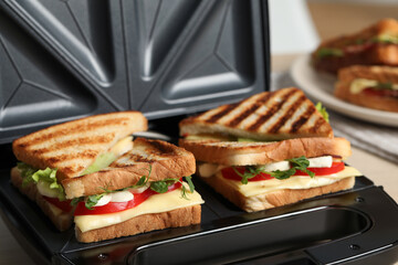 Modern grill maker with sandwiches on table, closeup view