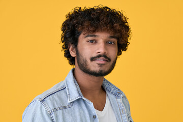 Young curly smart indian cool guy standing isolated on yellow background. Ethnic cool handsome man wearing denim shirt looking at camera posing for headshot close up face portrait. - obrazy, fototapety, plakaty