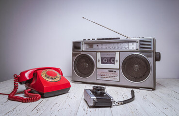 An old retro tape recorder, telephone and camera are on a wooden table