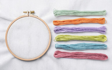 Threads near embroidery hoop with white fabric, flat lay