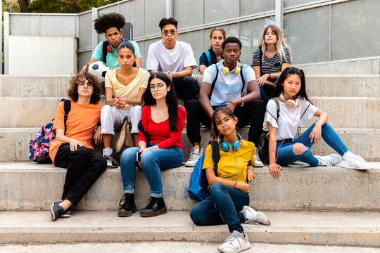 Multiracial Teenage Students Sitting On Steps In High School Outside Looking At Camera With Serious Expression.