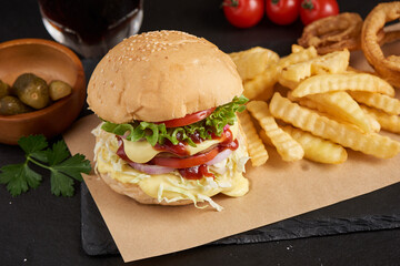 Homemade hamburger or burger with fresh vegetables and cheese lettuce and mayonnaise served, French fries on pieces of brown paper on black stone table . concept of fast food and junk food
