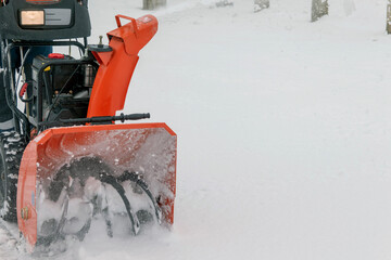 A man clears or removes snow with a snow blower on a snowy road near a high voltage transformer.