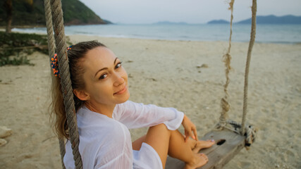 Woman on the swing on tropical beach. The girl in white shirt en