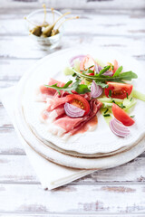 Plate of smoked ham with tomatoes and rocket. Bright wooden background.