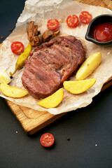 Beef steak with twig rosemary and potatoes on a wooden table.