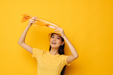 Charming young Asian woman in a hat with an airplane in his hands model toy yellow background unaltered