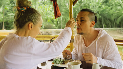 Man and woman eat and drink tasty beverages spending time in traditional local floating cafe on water. Loving happy couple having breakfast outdoors