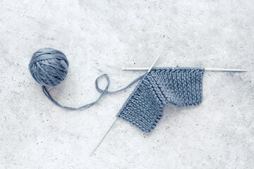 Piece of knitting, ball of yarn and a knitting needleson a gray concrete background