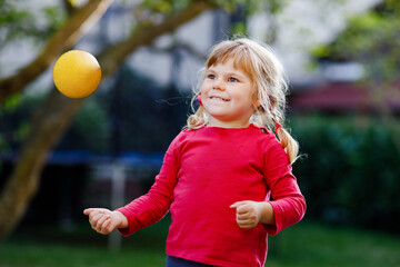 Little adorable toddler girl playing with ball outdoors. Happy smiling child catching and throwing, laughing and making sports. Active leisure with children and kids.