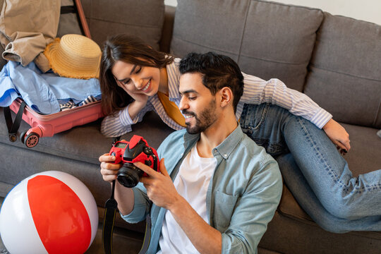 Loving spouses prerating for vacation, packing suitcase and using camera for watching photos in trip