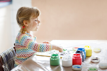 Little creative toddler girl painting with finger colors an owl bird. Active child having fun with drawing at home, in kindergaten or preschool. Games, education and distance learning for kids